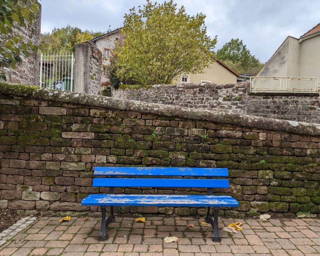 Eine knallblaue Parkbank vor einer alten, schiefen Mauer.