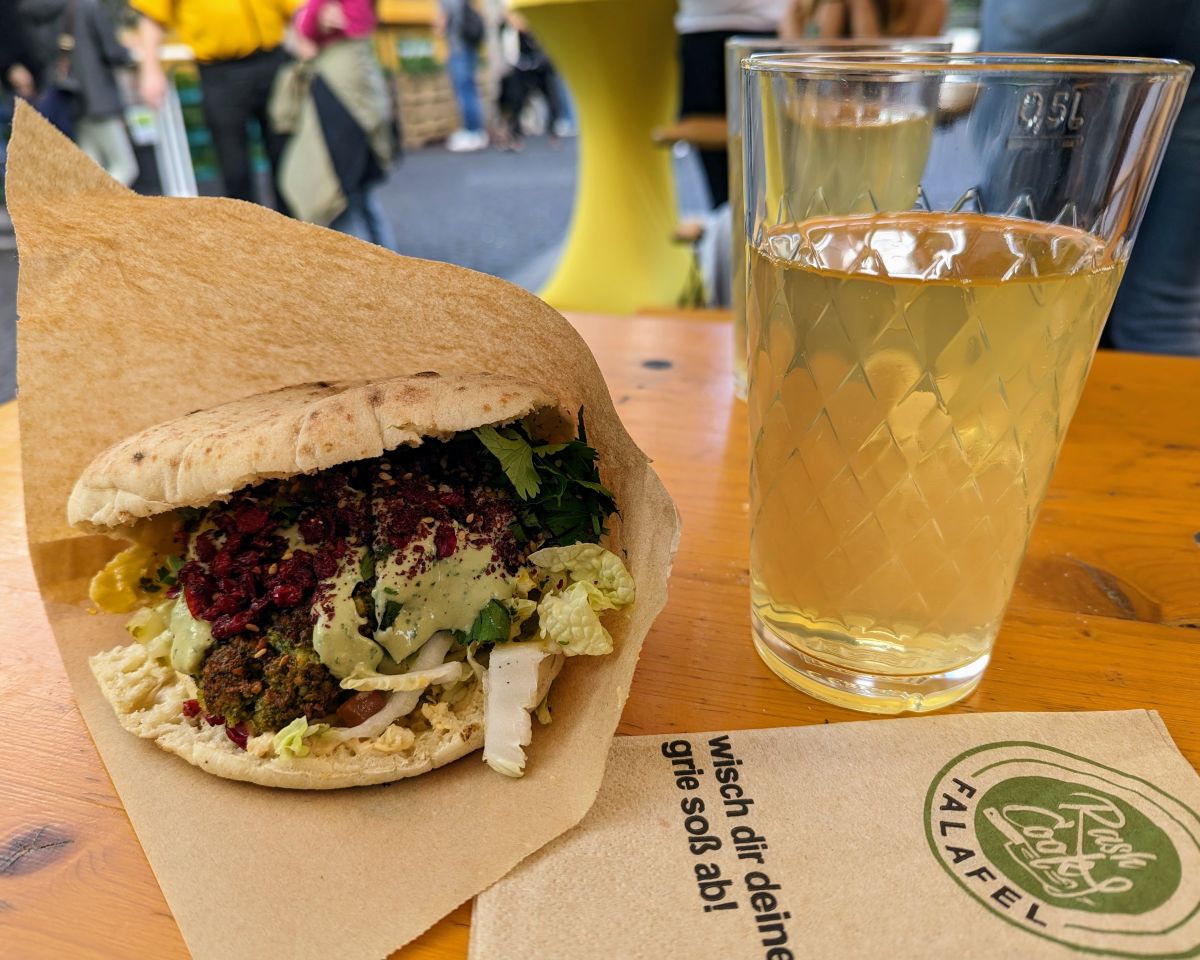 Foto von einem leckeren Falaffelsandwich mit grüner Soße, daneben ein Glas Apfelwein.