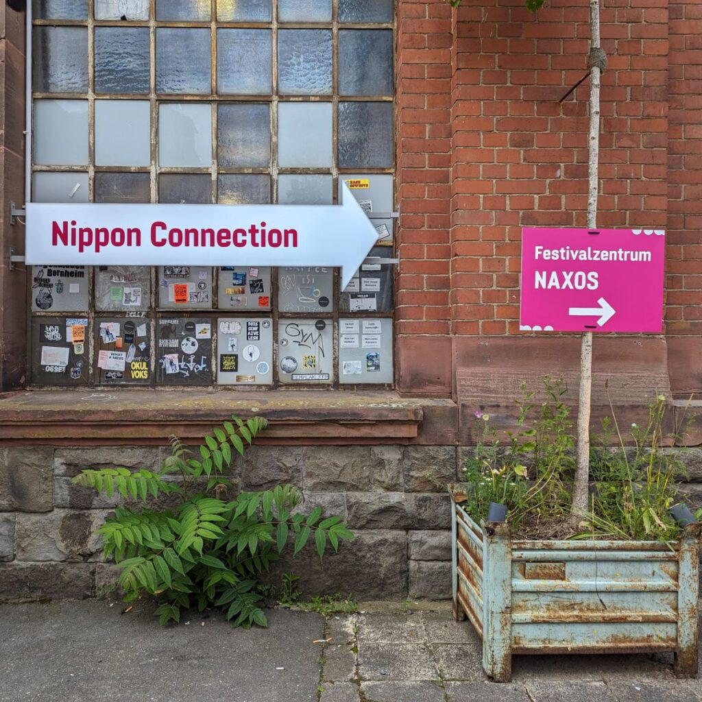 Bild von Nippon Connection Schildern vor der schrabbeligen Fassade der Naxoshalle