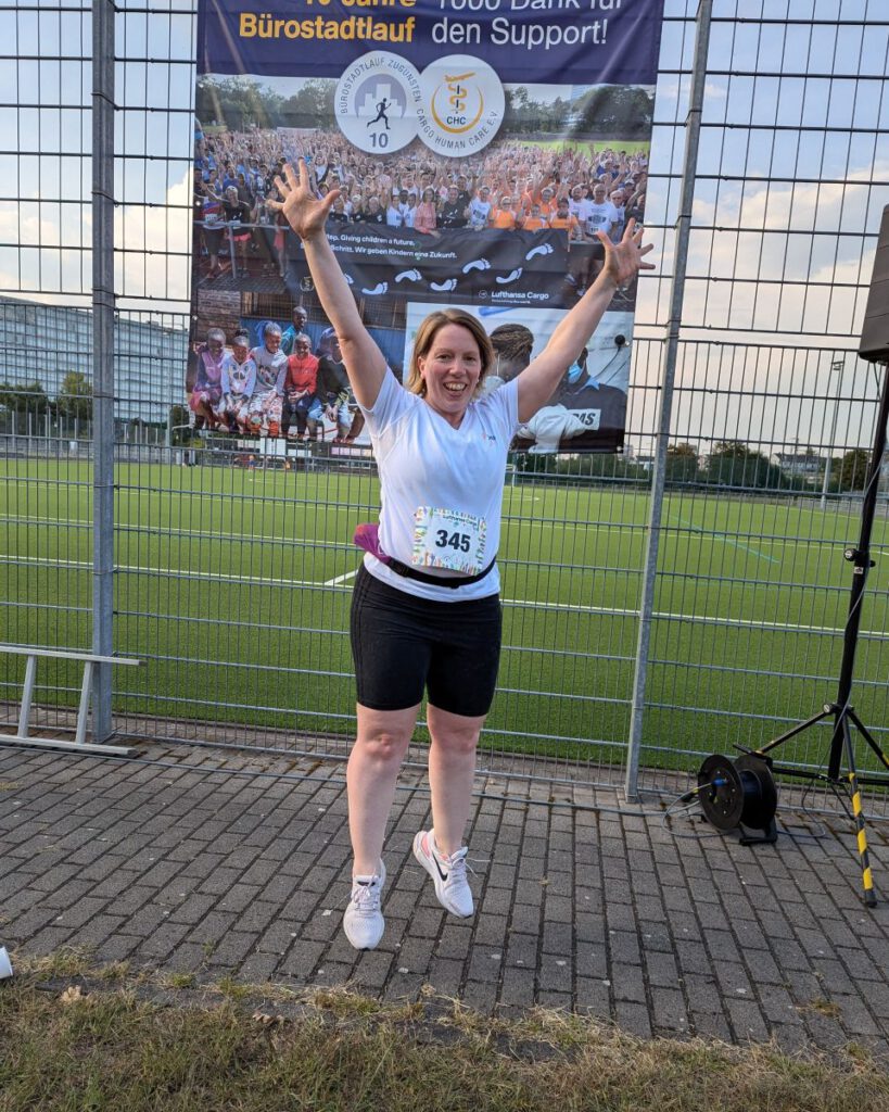 Astrid im Sportdress und mit Startnummer hüpft vor einem Schild "10 Jahre Bürostadtlauf" auf und ab.