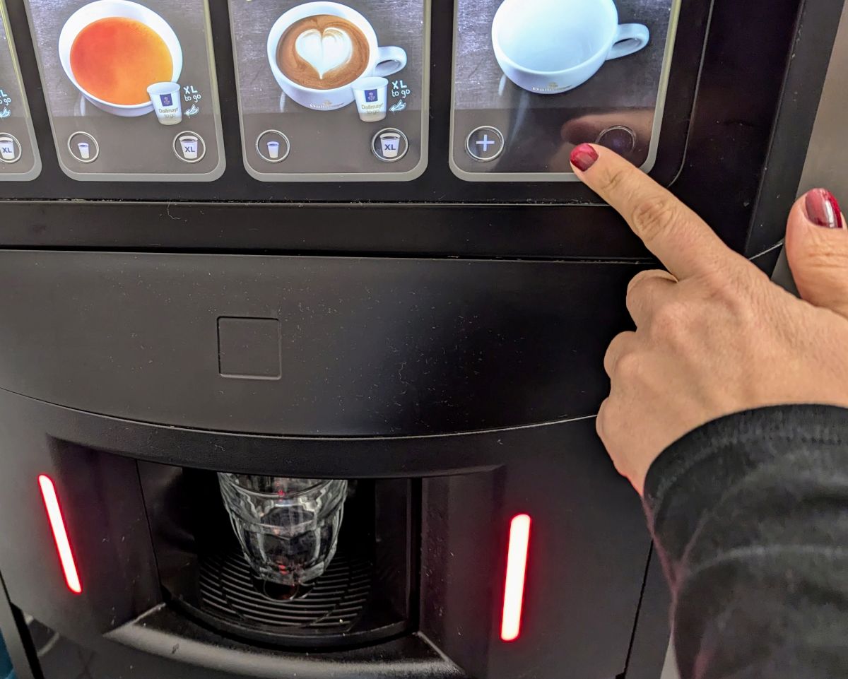 Hand die am Kaffeeautomaten die Taste für die eigene Tasse bedient.