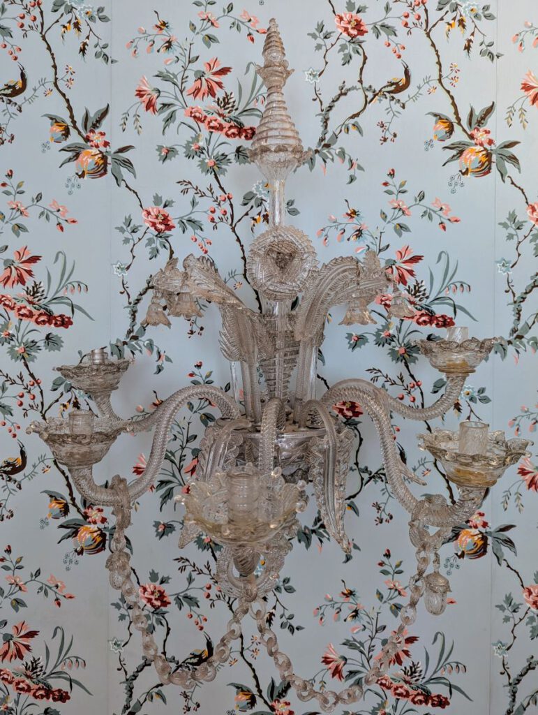 Kunstvoller Glas-Lüster auf einer hellblauen Tapete mit zartem Blütenmuster im Zimmer von Cornelia Goethe.