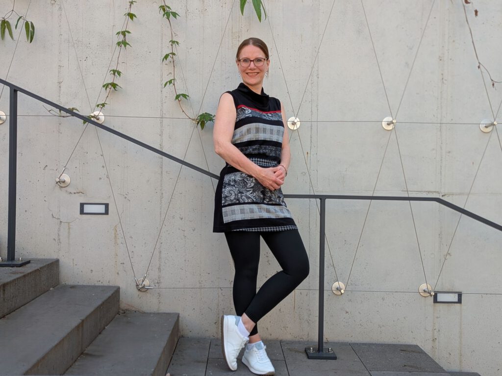 Maren Hünnerscheidt steht locker auf einer Treppe und blickt offen und lächelnd in die Kamera, ihre weißen Turnschuhe blitzen auf dem grauen BetonIm Hintergrund ranken zarte Blätter.