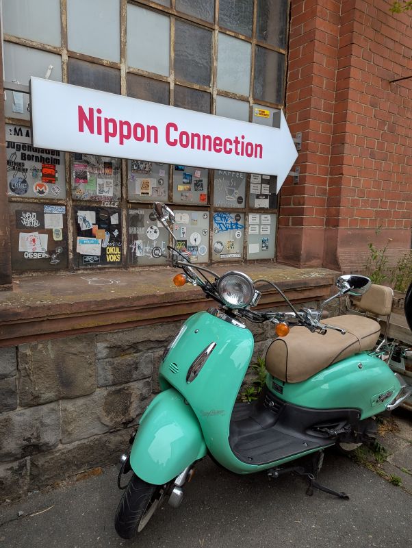 Türkisfarbene Vespa, die vor dem Nippon Connection Schild gepartk wurde.