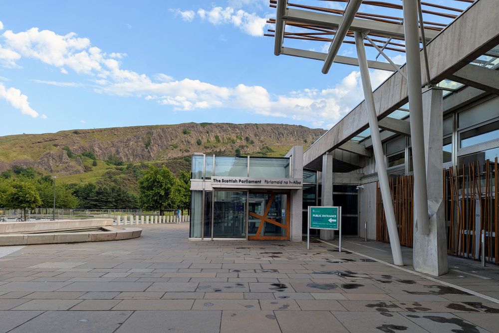Eingang des Scottish Parliament mit Park und Felsenwand im Hintergrund.
