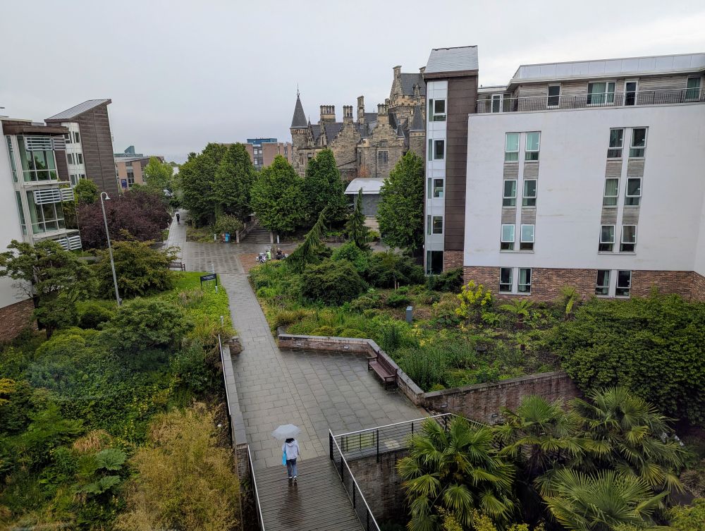Blick über den St. Leonards Hall Campus, es regnet, eine Frau ist mir Schirm unterwegs.