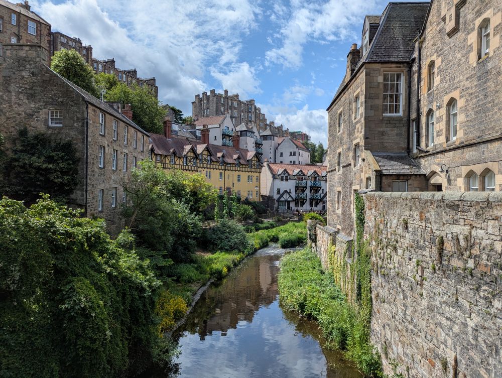 Malerische Ansicht des Water of Leith: Unten fließt der Fluß und auf beiden Seiten stehen alte Ssandsteinbauten in der Ferne auf dem Hügel steht ein großes Herrenhaus.