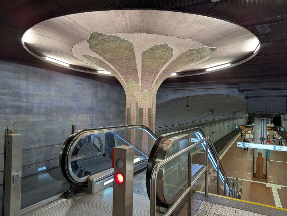 Haltestelle Westend mit einer als Blütenunterseite oder Pilz gestalteter Säule neben der Rolltreppe nach unten.