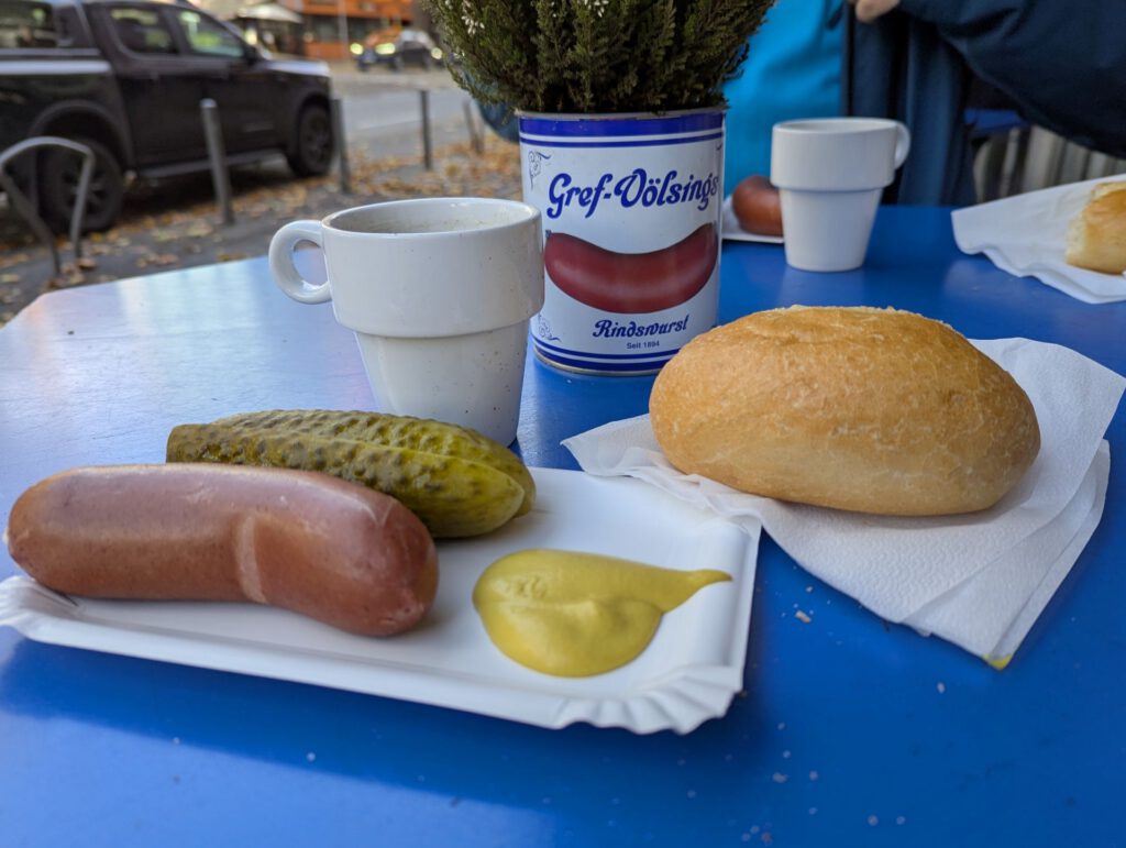 Ein Frankfurter Gedeck: Besteht aus einer Rindswurst, einem Wasserweck mit einem Becher Brühe und einer Salzgurke.