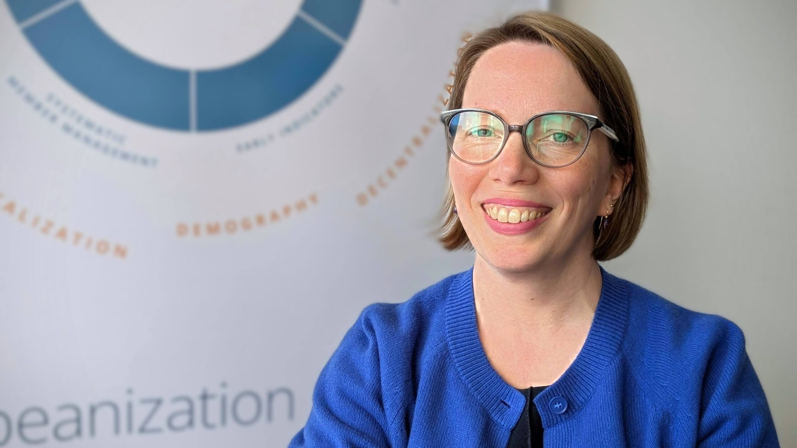 Astrid Schewe trägt eine knallblaue Strickjacke und lächelt breit in die Kamera