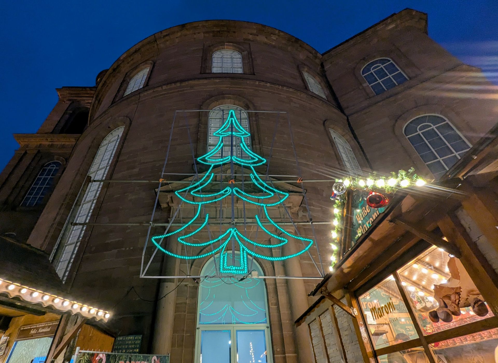 Die Frankfurter Paulskirche am Abend. Über dem Eingang hängt ein Lichter-Weihnachtsbaum, davor sieht man im zwei beleuchtete Weihnachtsmarktstände.